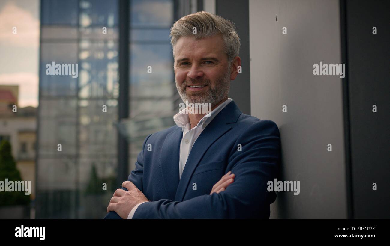 Ritratto d'affari all'aperto datore di lavoro dai capelli grigi in posa in città uomo d'affari caucasico di mezza età, uomo d'affari, incrociato le mani con le braccia vicino all'azienda Foto Stock