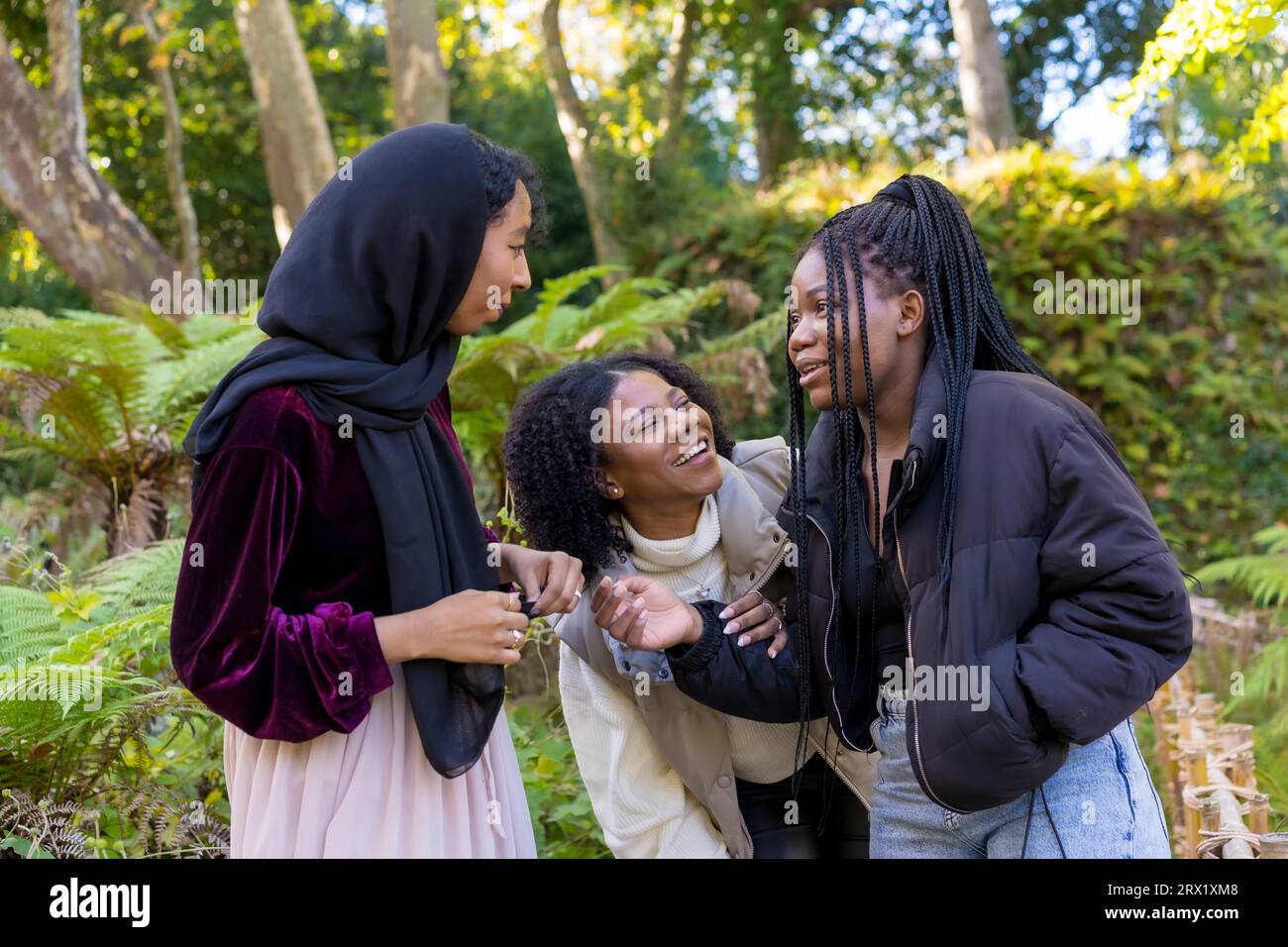 Foto orizzontale di una giovane donna musulmana e di amiche afroamericane che ridono in un parco Foto Stock