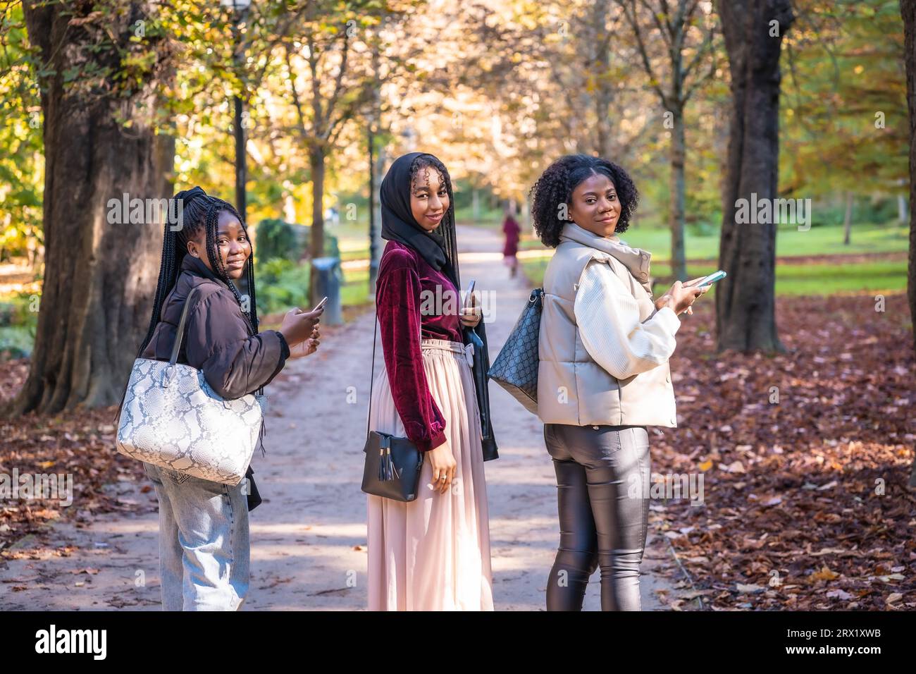 Tre amici multiculturali che sorridono davanti alla telecamera mentre camminano lungo un parco Foto Stock