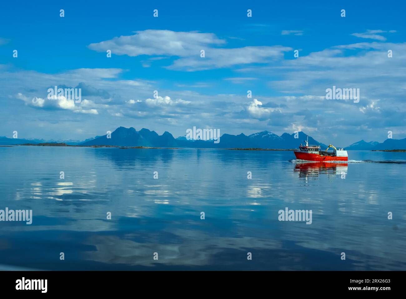 Barca da pesca rossa che naviga sull'acqua con montagne in lontananza vicino a Svolvaer in Norvegia Foto Stock