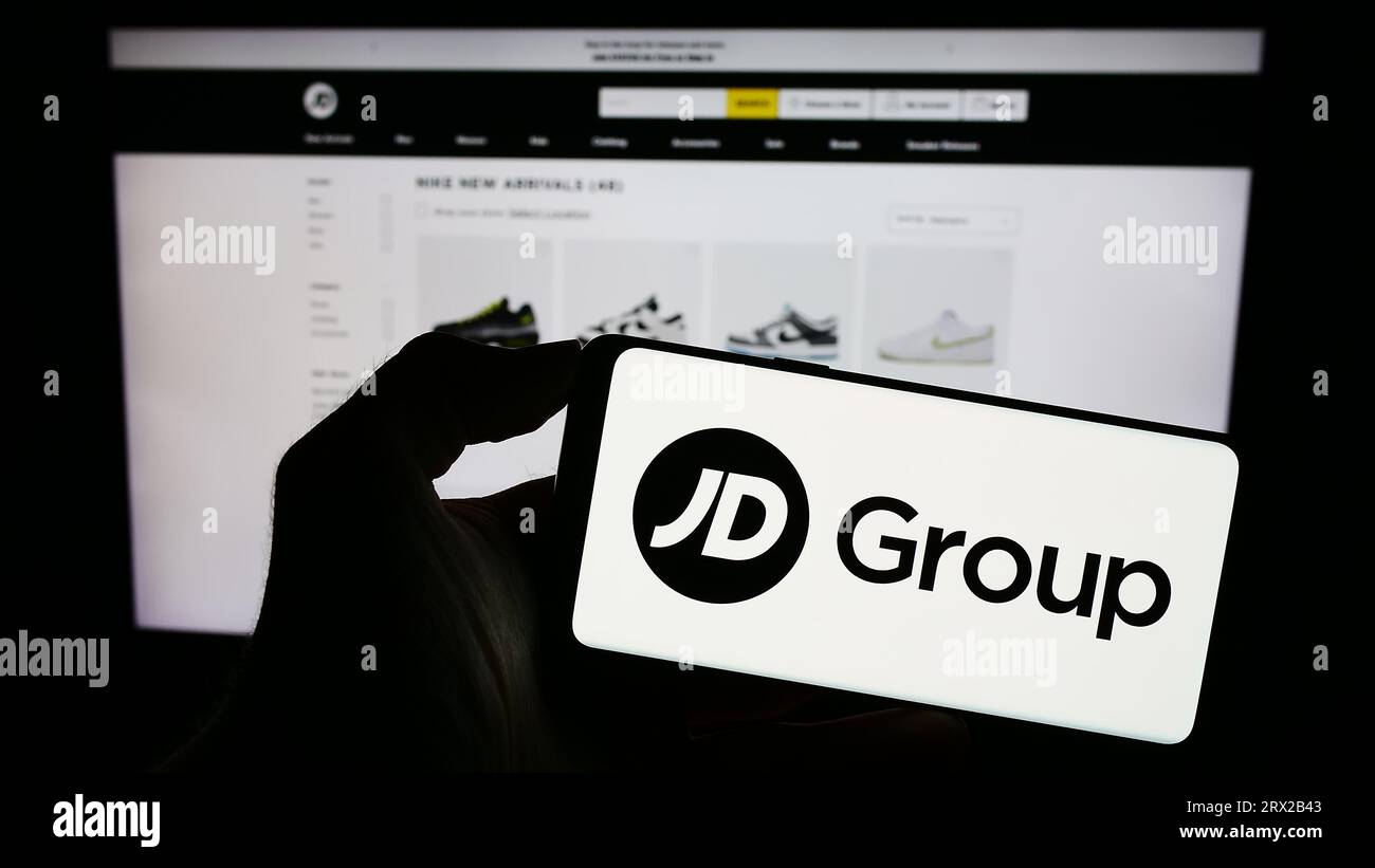 Persona che possiede uno smartphone con il logo della società di vendita al dettaglio britannica JD Sports Fashion plc sullo schermo di fronte al sito Web. Concentrarsi sul display del telefono. Foto Stock