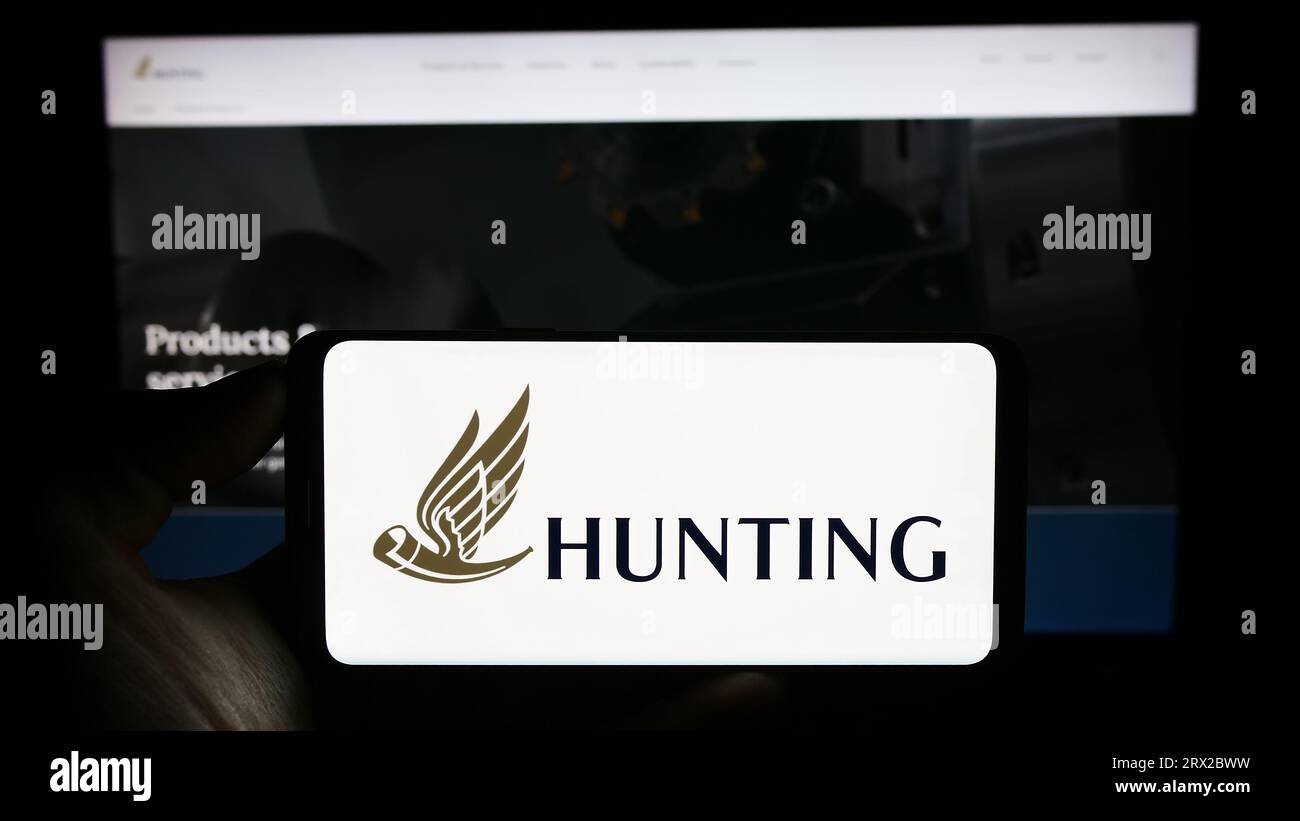 Persona che possiede un telefono cellulare con il logo della società britannica di tecnologia energetica Hunting plc sullo schermo davanti alla pagina Web. Concentrarsi sul display del telefono. Foto Stock