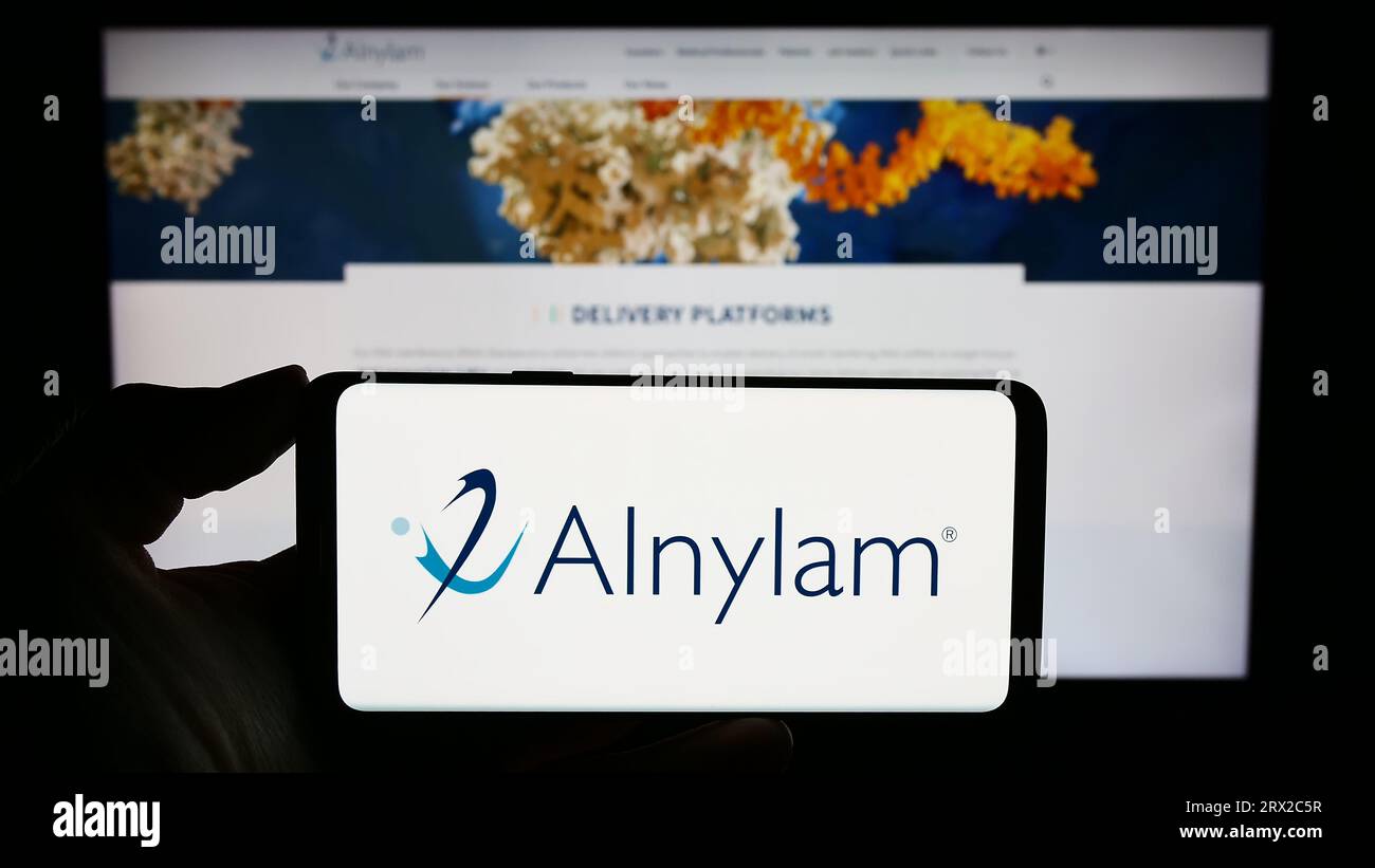 Persona che possiede uno smartphone con il logo della società statunitense Alnylam Pharmaceuticals Inc. Sullo schermo di fronte al sito Web. Concentrarsi sul display del telefono. Foto Stock