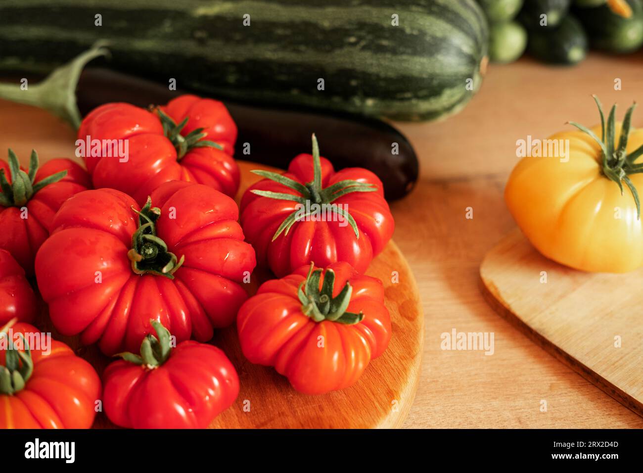 Pomodori grandi maturi, melanzane, verdure su un locale di lavoro in legno della cucina. Molte verdure crude di fondo. Pomodoro, cetrioli. Fornello a casa che fa una h Foto Stock