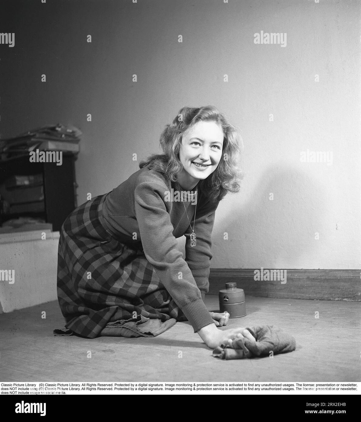 Una donna nel passato. Una donna si inginocchia sul pavimento e pulisce il tappeto con un panno. Svezia 1945. Kristoffersson rif M4-1 Foto Stock