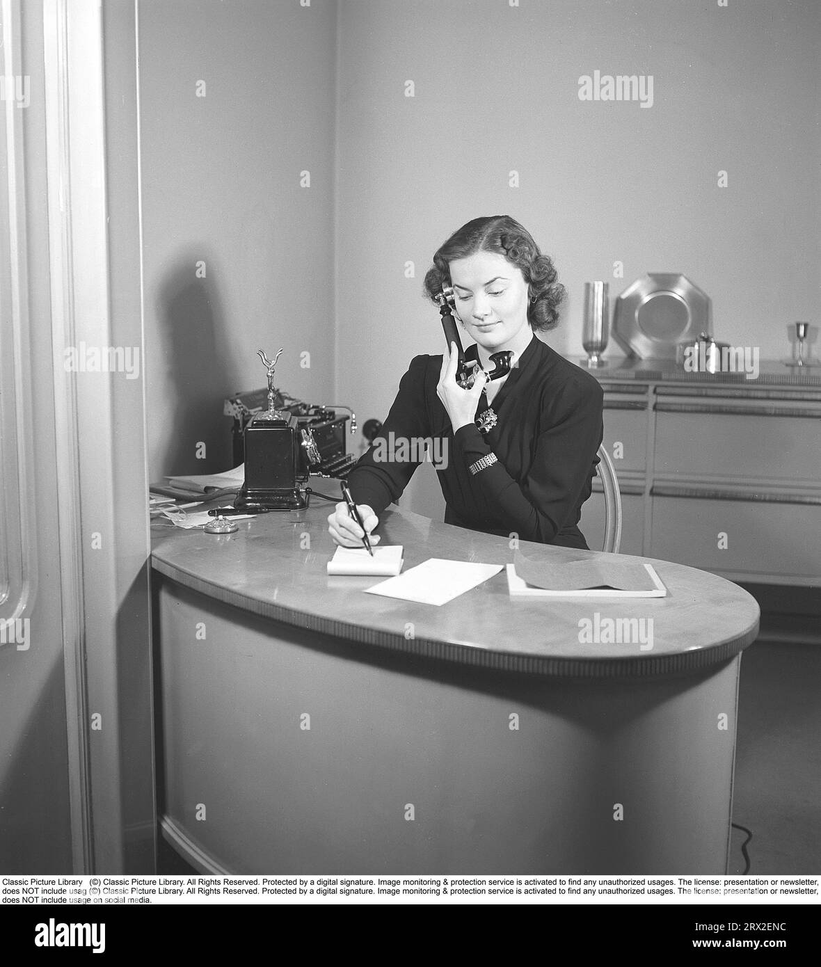 Donna negli anni '1940 Interno di un ufficio dove una giovane donna siede a una scrivania e parla al telefono. È vestita in modo ordinato e prende appunti mentre parla al telefono. Svezia 1945. Kristoffersson rif. M107-2 Foto Stock