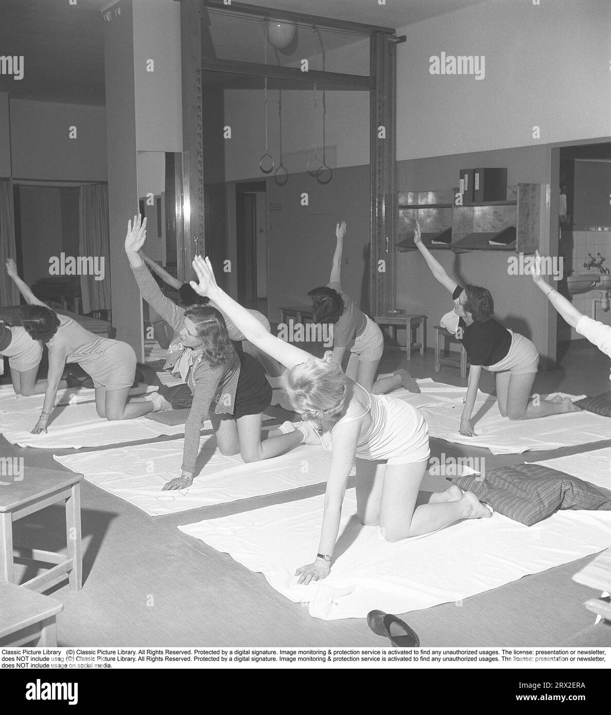 Ginnastica in passato. In una palestra, un gruppo di donne si inginocchiano e allungano le braccia in un movimento. Le giovani donne si prendono una pausa dal lavoro e fanno ginnastica durante l'orario di lavoro. La ginnastica da ufficio era un'invenzione moderna negli anni '1940, quando l'assistenza sanitaria per i dipendenti cominciò ad essere implementata. Svezia 1949. Kristoffersson rif. AX72-7 Foto Stock