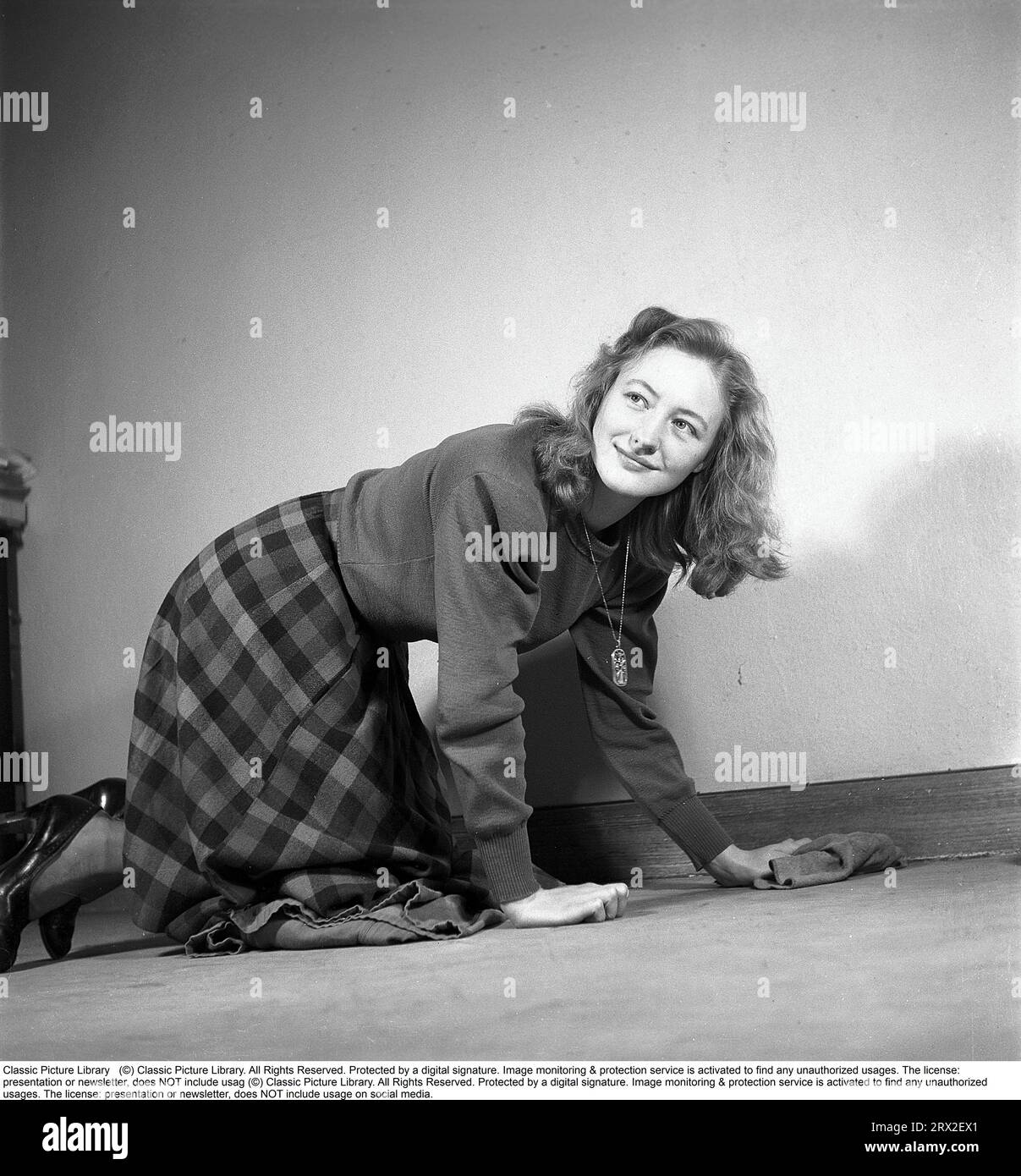 Una donna nel passato. Una donna si inginocchia sul pavimento e pulisce il tappeto con un panno. Svezia 1945. Kristoffersson rif M3-6 Foto Stock