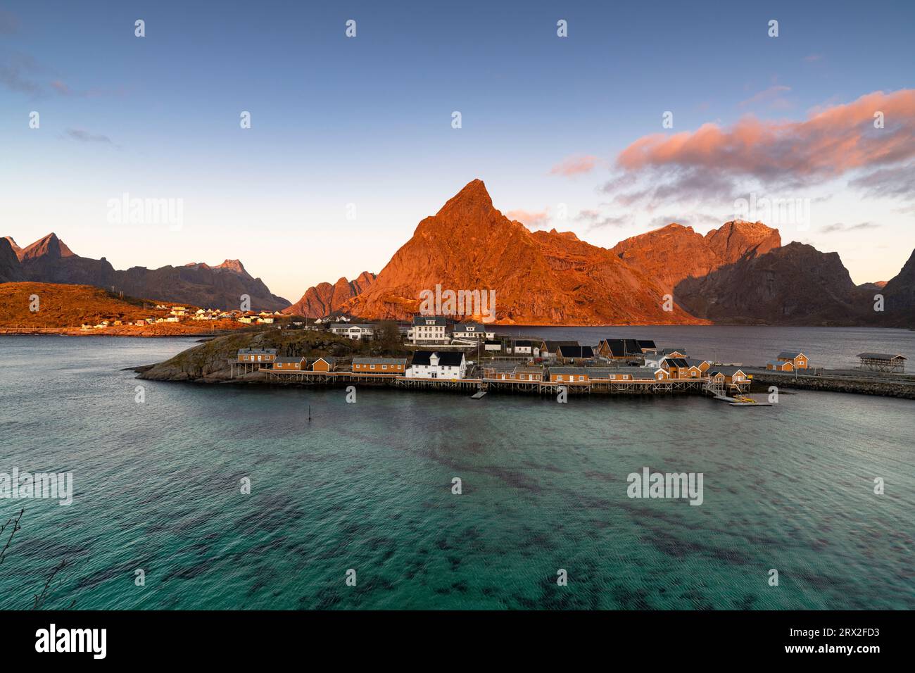 Alba sul monte Olstind e villaggio di pescatori di Sakrisoy, affacciato sul mare cristallino, sulle isole Lofoten, sul Nordland, sulla Norvegia, sulla Scandinavia, Europa Foto Stock