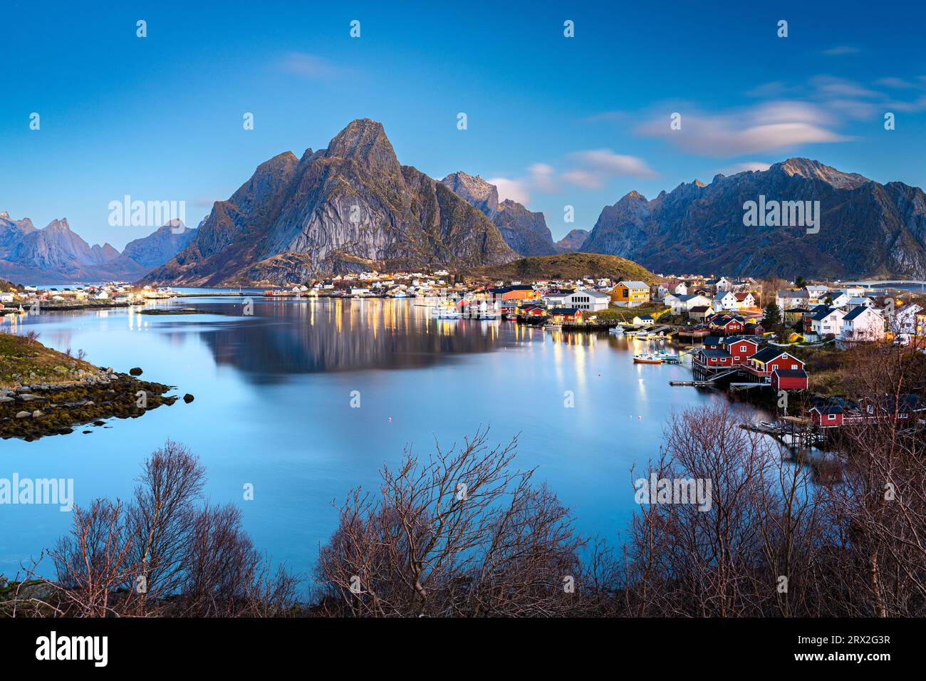 Crepuscolo sulla maestosa montagna Olstind che si affaccia sull'iconico porto del villaggio di pescatori di Reine, sulle isole Lofoten, sul Nordland, sulla Norvegia e sulla Scandinavia Foto Stock