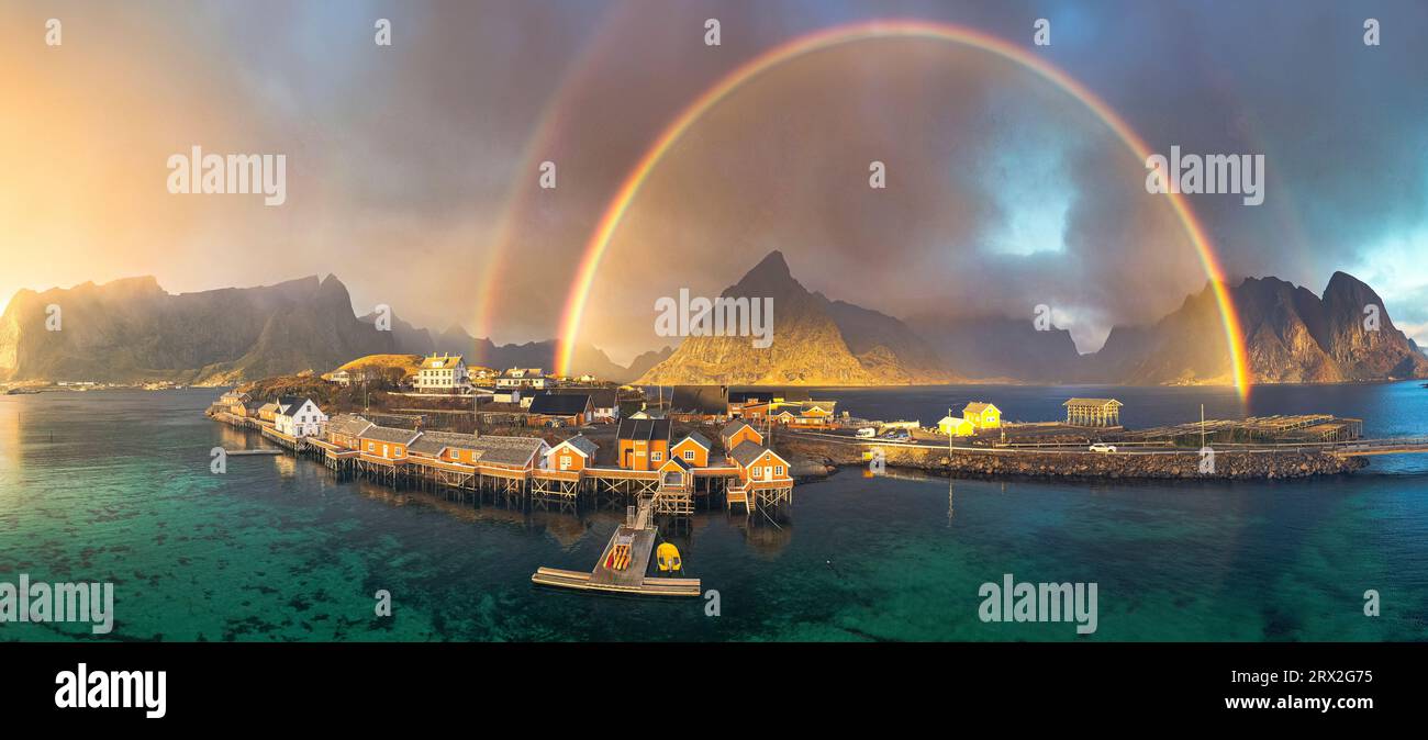 Vista aerea degli idilliaci arcobaleni sul monte Olstind e delle capanne dei pescatori sul mare, Sakrisoy, Reine, Isole Lofoten, Nordland, Norvegia, Scandinavia Foto Stock