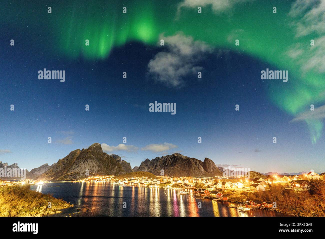 Porto illuminato di Reine riflesso nel freddo mare artico durante l'aurora boreale, Reine, Isole Lofoten, Nordland, Norvegia Foto Stock