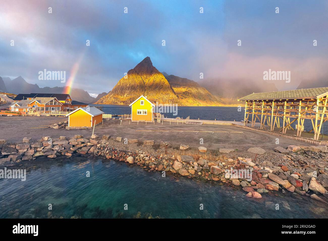 Vista panoramica aerea del tradizionale rorbu e del picco Olstind sotto l'arcobaleno, Sakrisoy, Reine, Isole Lofoten, Nordland, Norvegia, Scandinavia, Europa Foto Stock