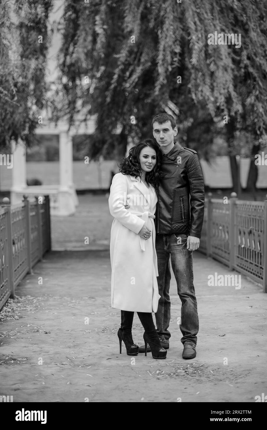 Un uomo abbraccia sua moglie incinta. Un uomo con una giacca nera abbraccia una donna con un cappotto bianco Foto Stock