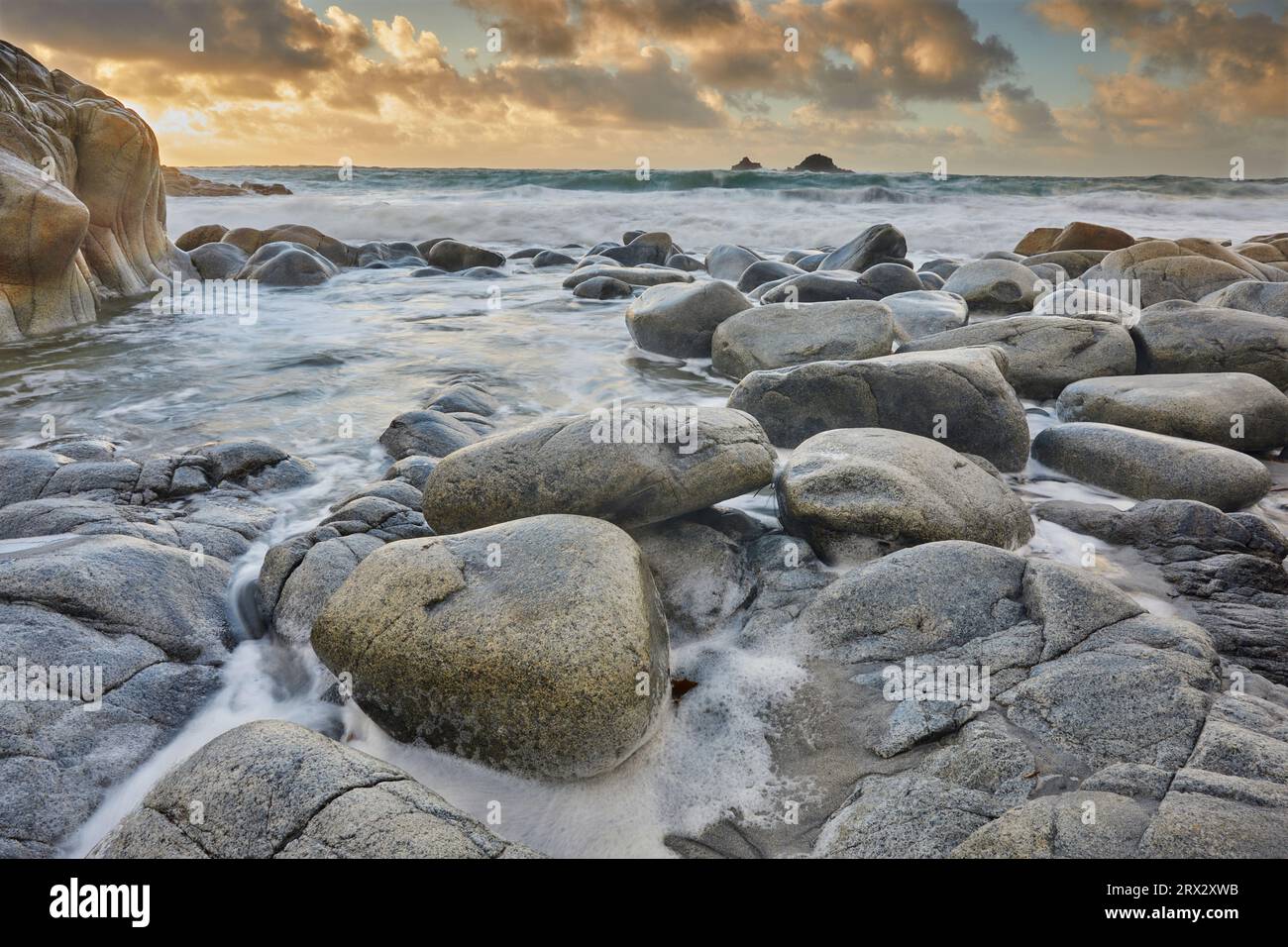 I rulli atlantici si innalzano intorno a massi di granito lungo la costa su una marea che si alza al tramonto, Porth Nanven, una remota insenatura vicino a St. Giusto Foto Stock