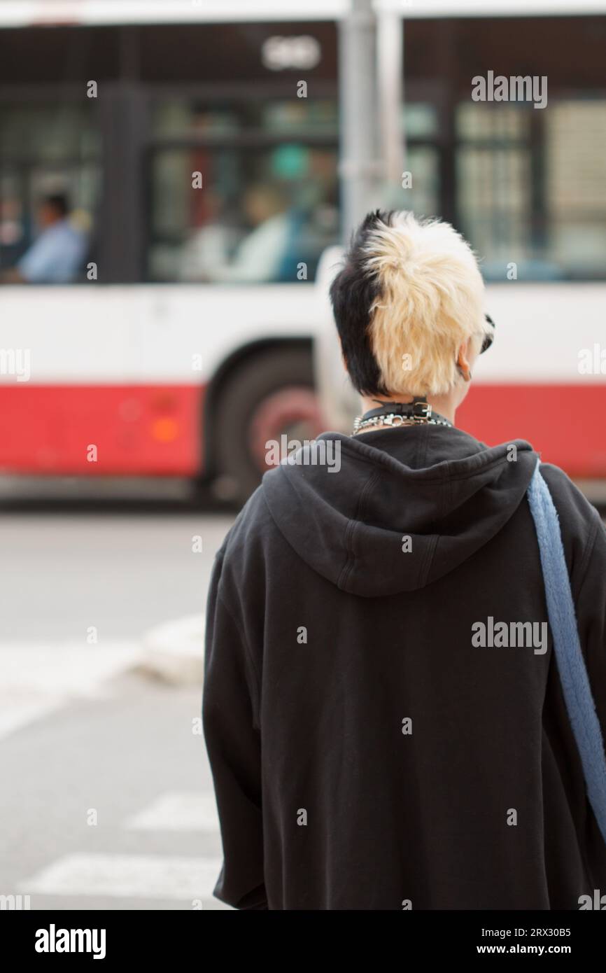Giovane donna con uno stile alternativo in attesa che il semaforo diventi verde ad Alicante e un autobus che passa sullo sfondo, Spagna Foto Stock