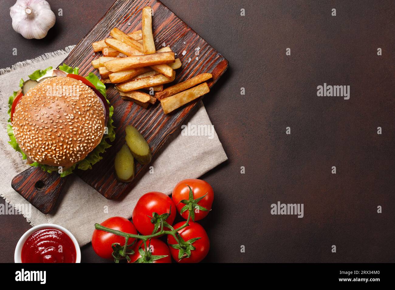 Hamburger fatti in casa con ingredienti di manzo, pomodori, lattuga, formaggio, cipolla, i cetrioli e le patatine fritte sul tagliere e rusty sfondo. Vista superiore Foto Stock