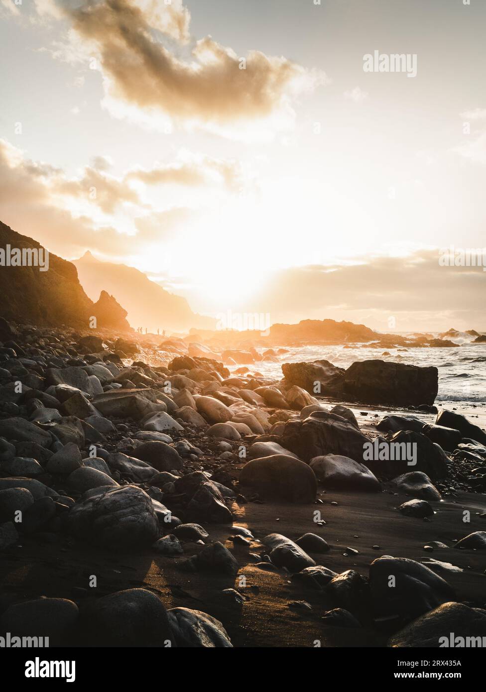 Splendida vista della spiaggia rocciosa e della scogliera lungo la costa nord di Tenerife al tramonto. Oceano Atlantico ondulato con sole dorato nelle Isole Canarie. Foto Stock