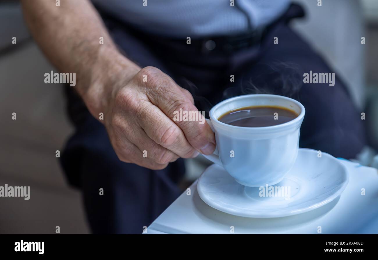 Il vecchio le mani reggono una tazza di caffè su camicie bianche Foto Stock