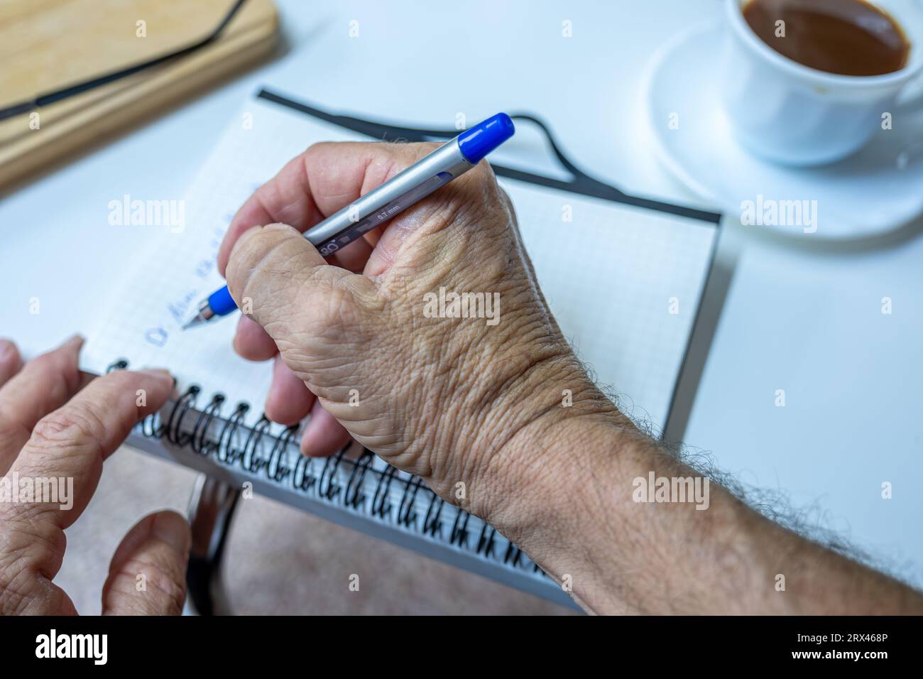 Il vecchio scrive appunti mentre beve caffè in salotto Foto Stock