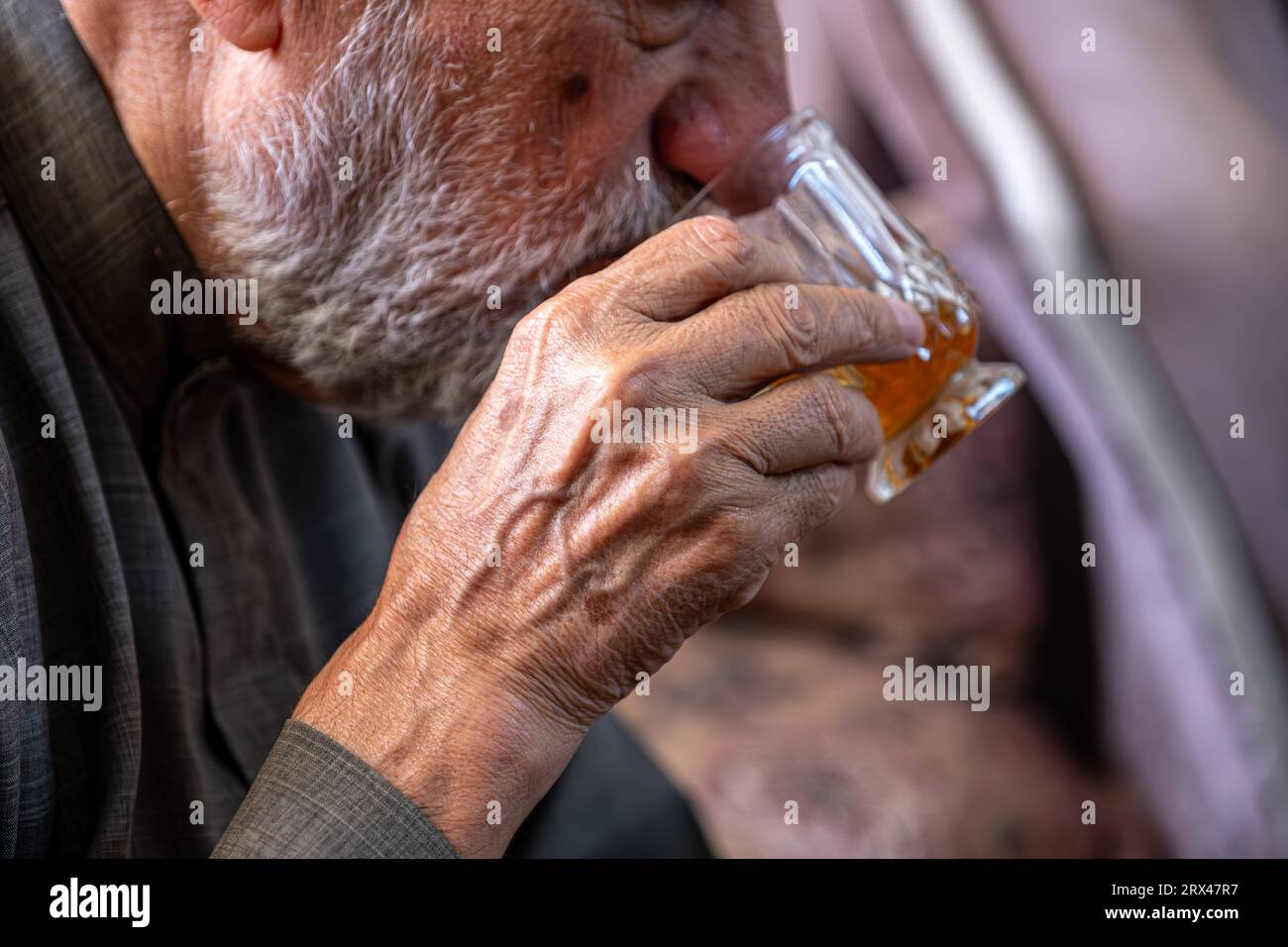 Vecchio arabo che beve tè e tiene un bicchiere di tè in mano Foto Stock