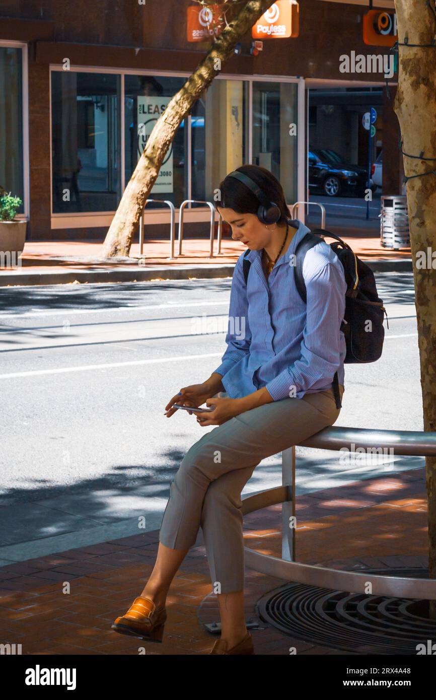 Giovane donna che ascolta le cuffie e guarda il telefono sul marciapiede nel centro di Portland, Oregon Foto Stock