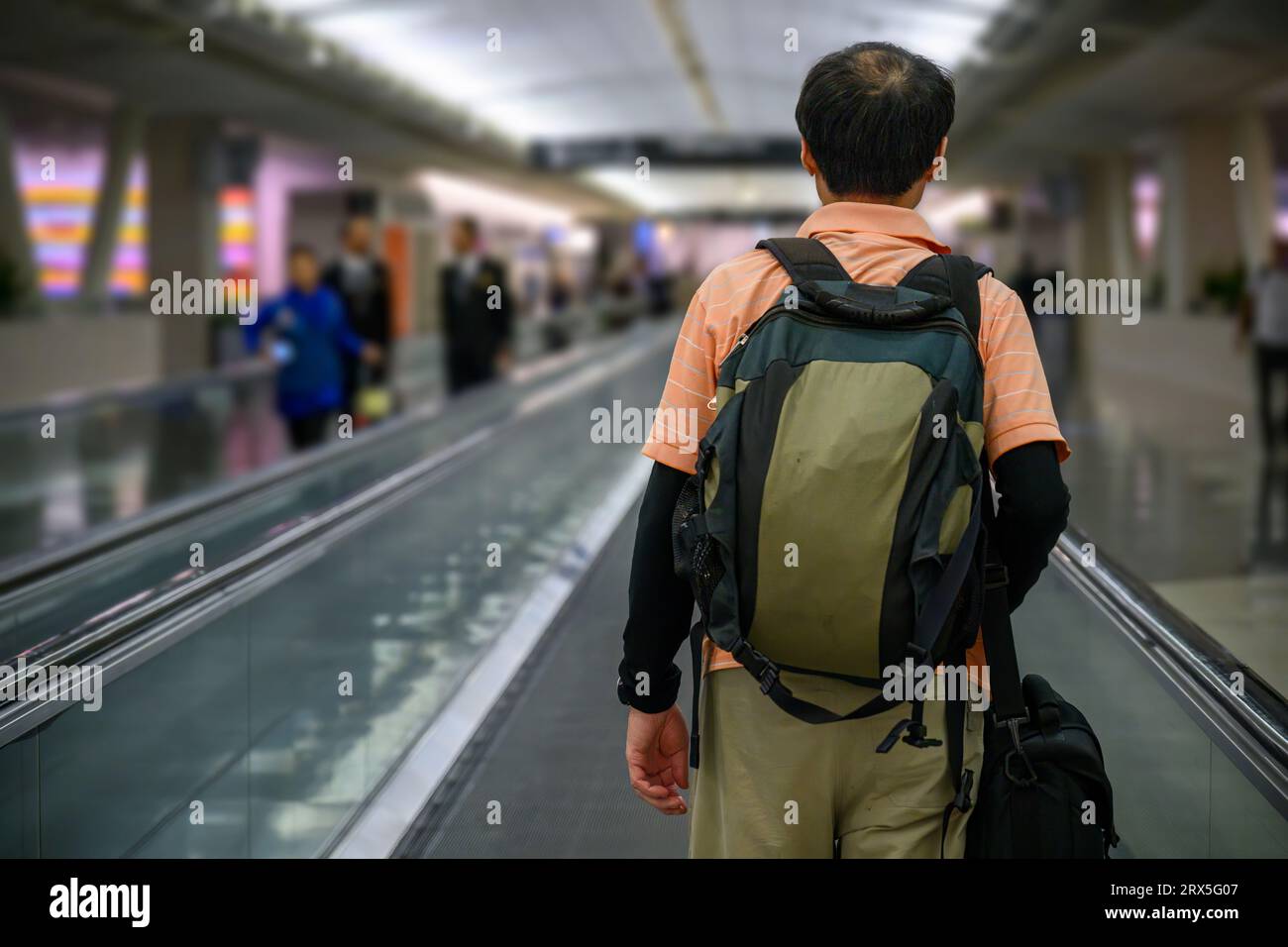 Uomo che cammina sul passaggio pedonale in un aeroporto. Persone non riconoscibili sullo sfondo. Foto Stock