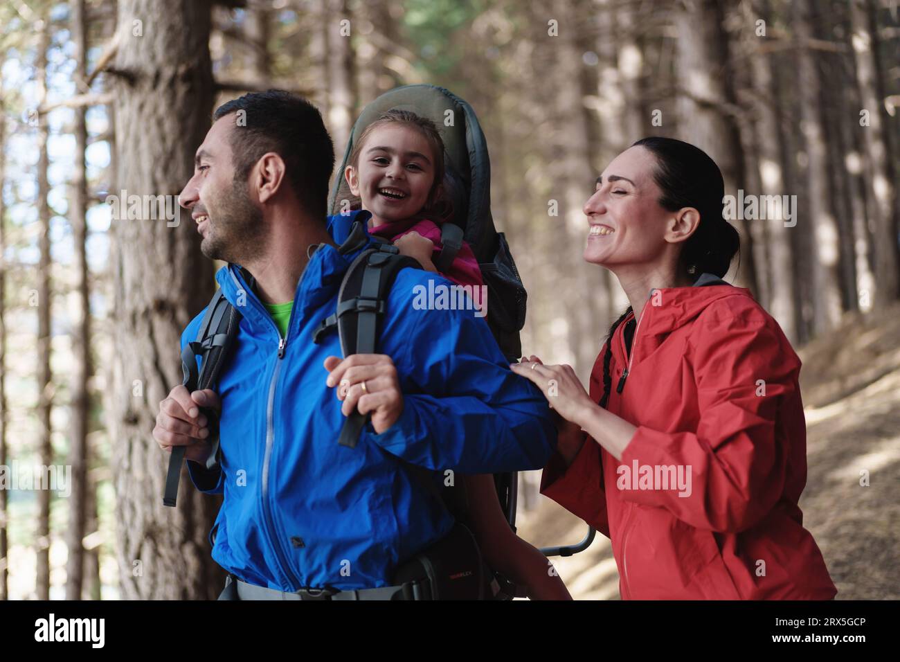 Deliziosa famiglia mediterranea, trekking nella foresta. Il padre porta la figlia in uno zaino specializzato per bambini, mentre esplorano nat Foto Stock