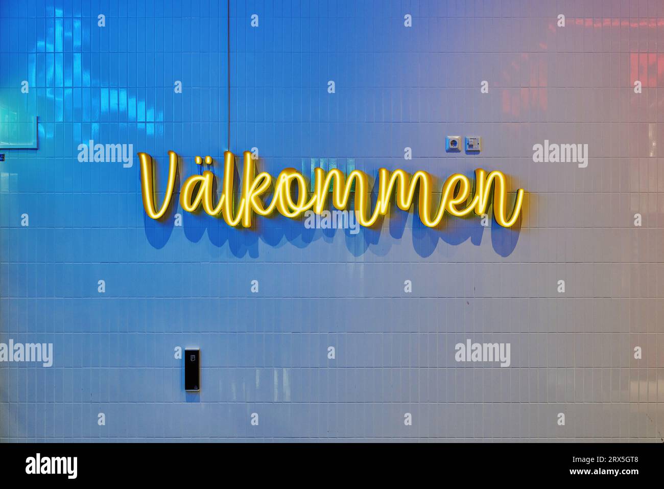 "Välkommen" (svedese: "Benvenuto"), insegna al neon sul muro piastrellato Foto Stock
