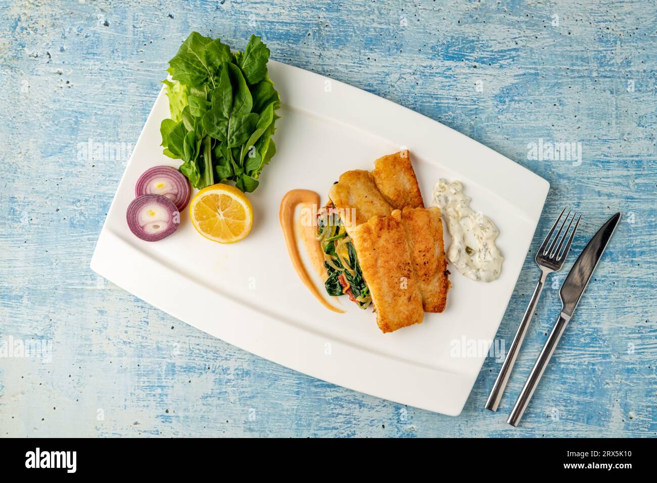 Filetto di panga fritto con verdure e cipolle sul lato e spinaci sottostanti Foto Stock