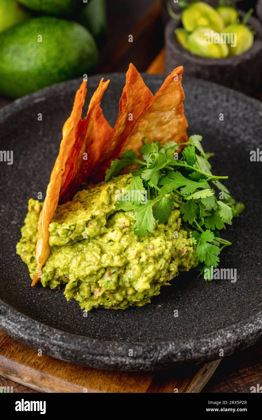 Guacamole all'avocado con tortillas croccanti su un piatto di pietra nera su un tavolo di legno Foto Stock
