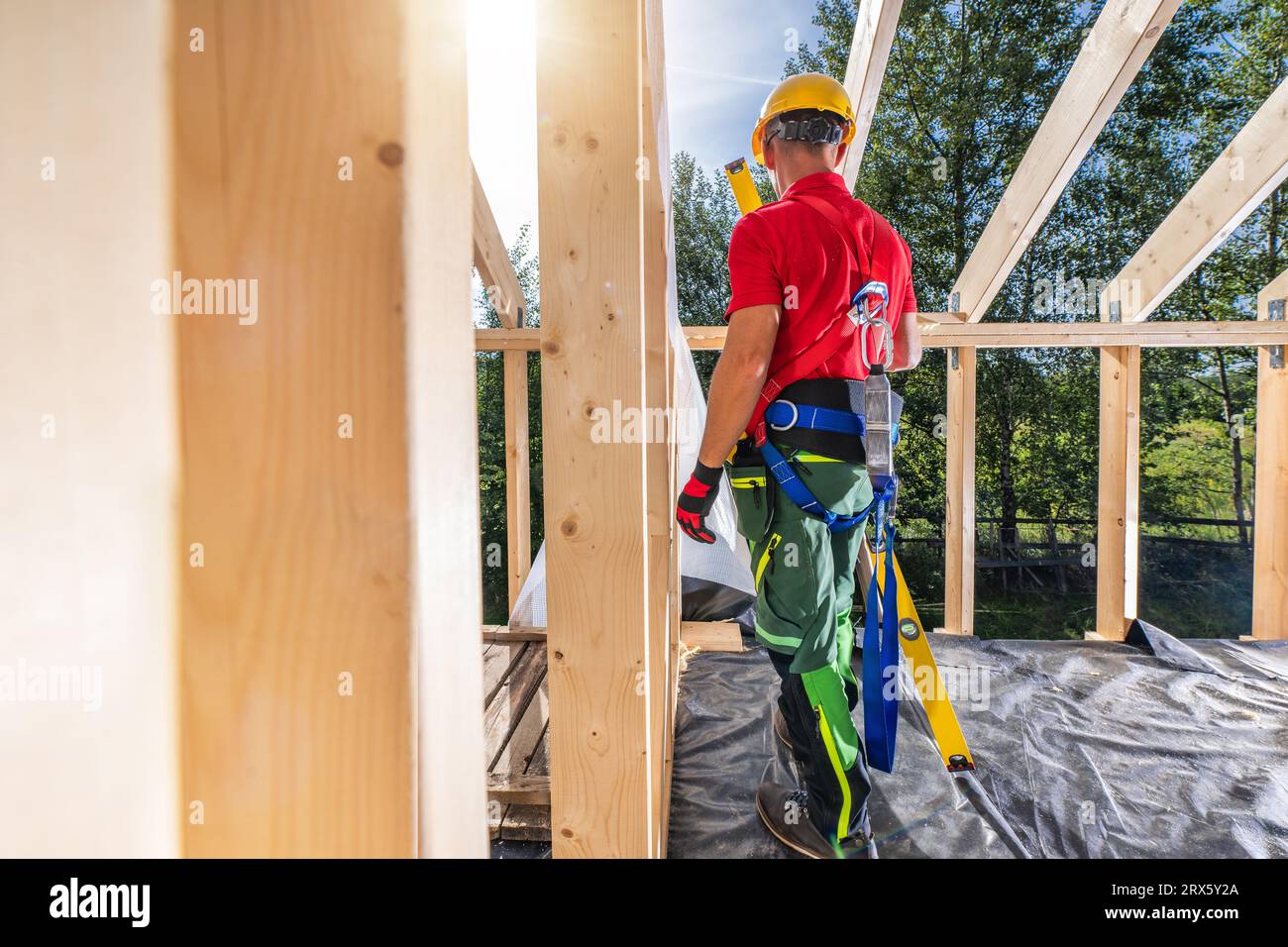 Appaltatore edile professionale che indossa imbracature di sicurezza all'interno di un telaio con scheletro in legno di nuova costruzione Foto Stock
