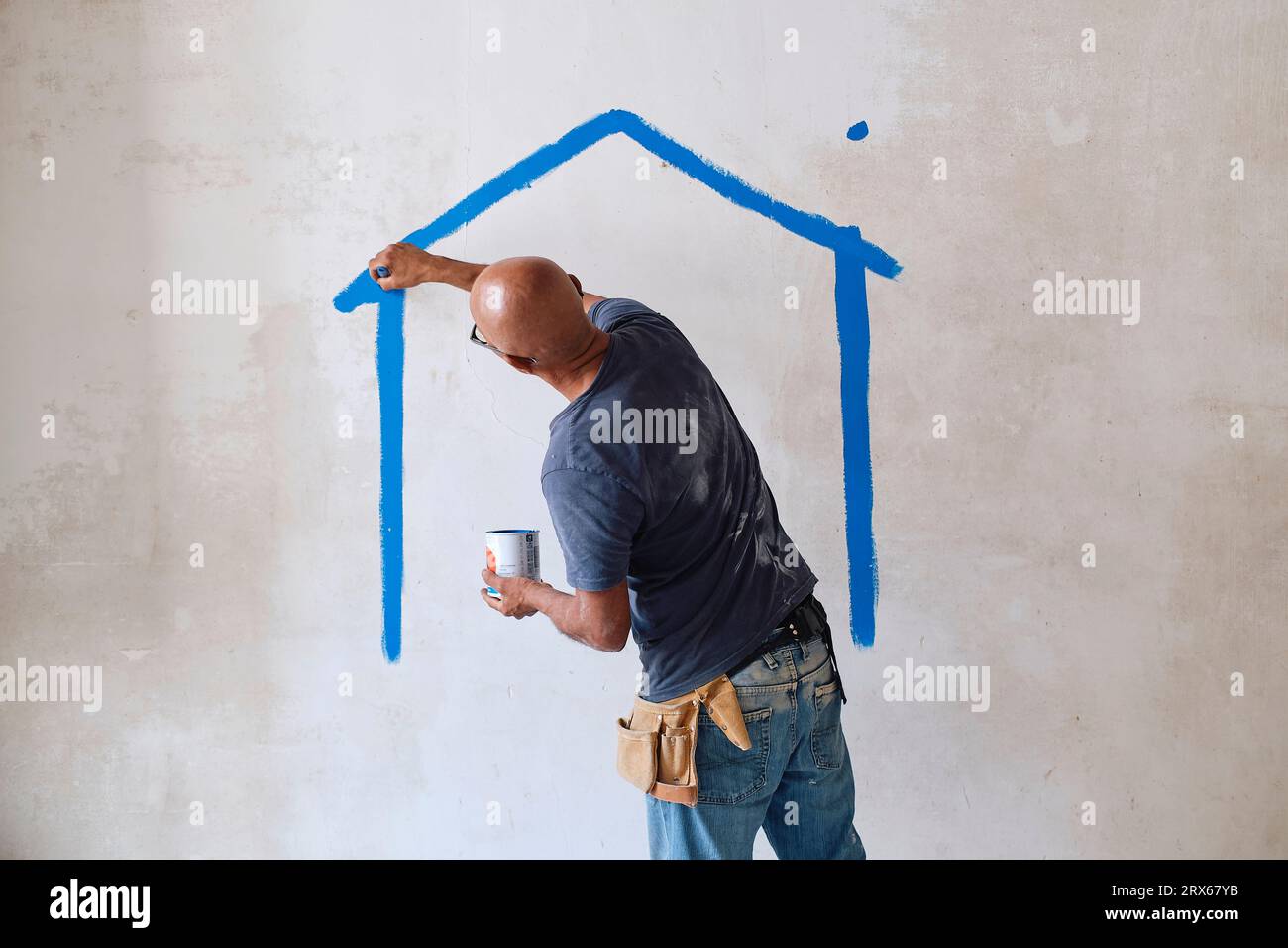 Lavoratore edile calvo disegna la casa sulla parete con pennello in loco Foto Stock