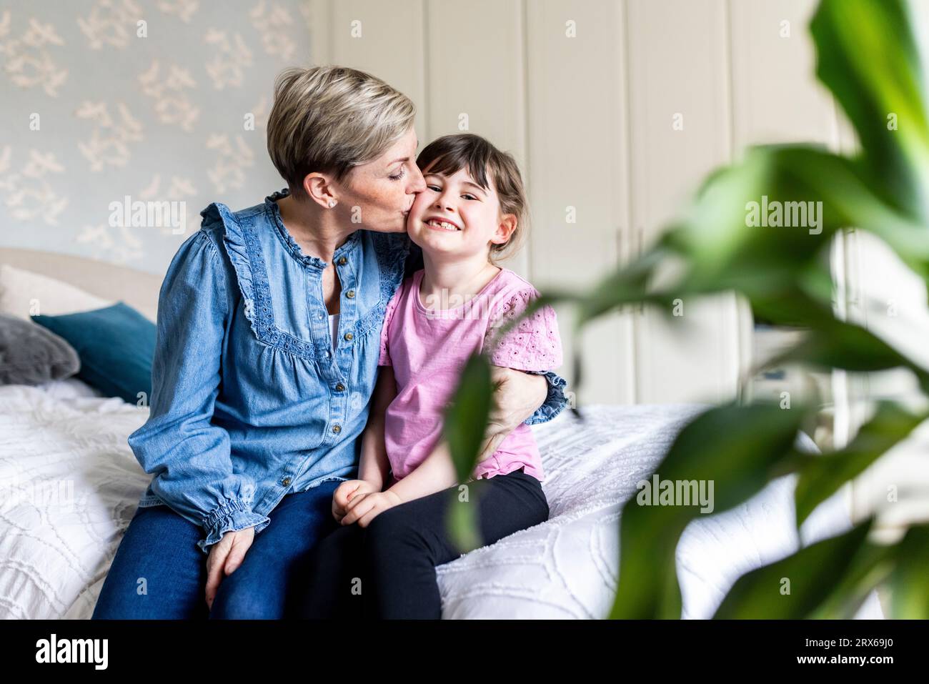 Donna matura che bacia figlia seduta sul letto a casa Foto Stock