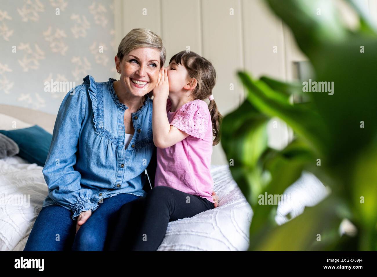 Ragazza che sussurra nell'orecchio sorridente della madre in camera da letto Foto Stock