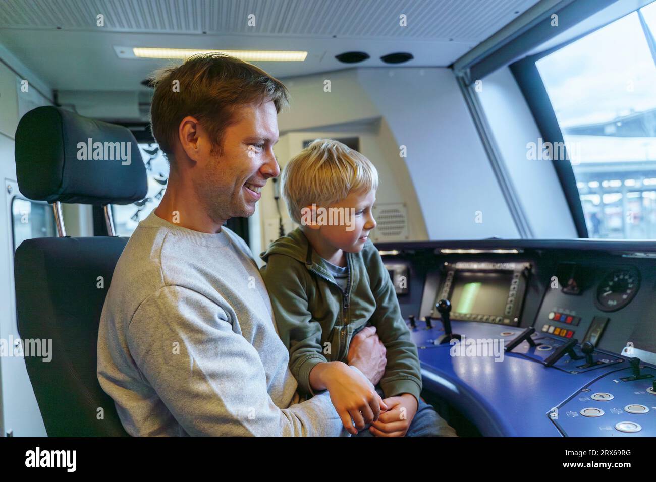 Un uomo con un aspetto europeo di 40 anni e suo figlio biondo di 5 anni siedono nella cabina del conducente del treno Foto Stock