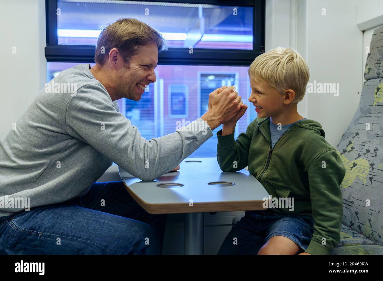 Padre e figlio felici che lottano a braccio sul tavolo in treno Foto Stock