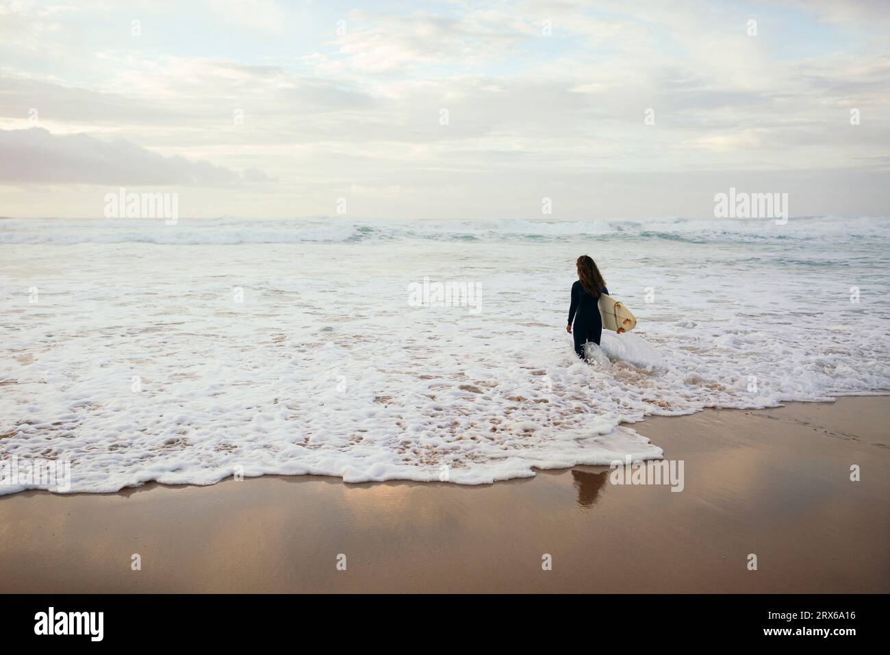 Giovane surfista con tavola da surf che cammina in mare ondulato in spiaggia Foto Stock