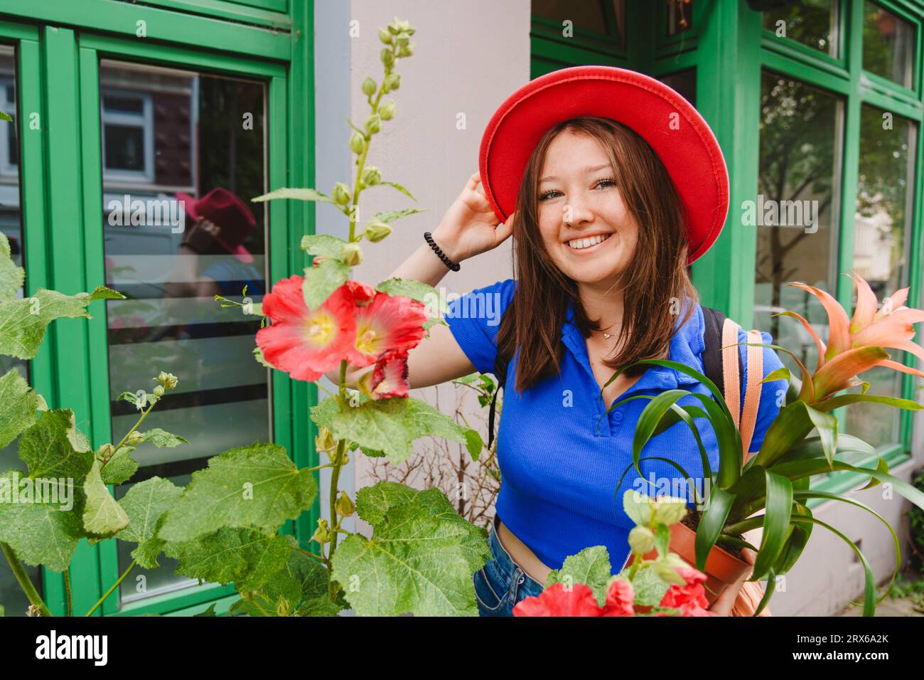 Ragazza adolescente sorridente con una pianta in vaso accanto ai fiori di Hollyhock Foto Stock