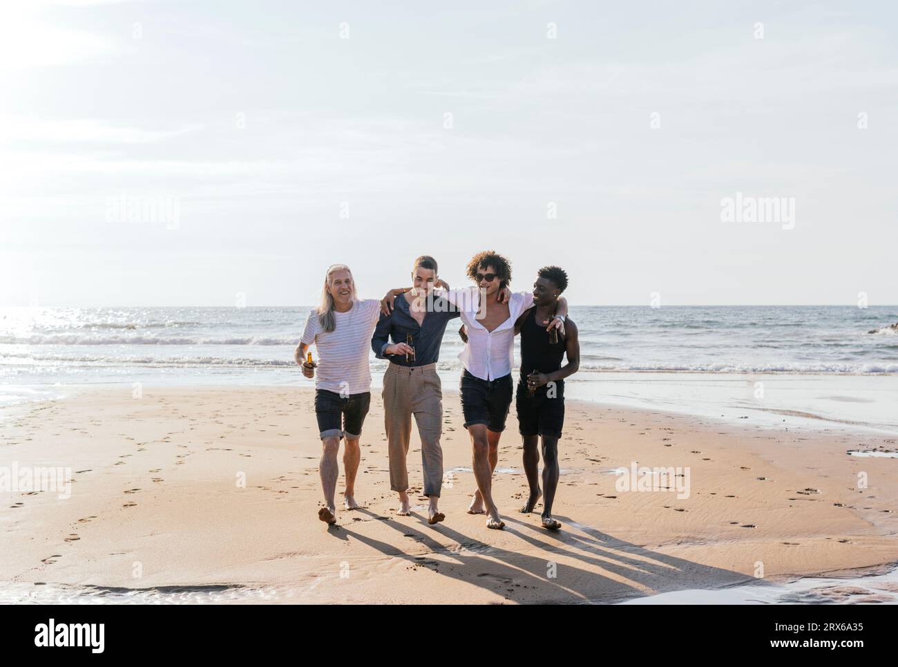 Amici multietnici con le braccia in giro a piedi in spiaggia Foto Stock