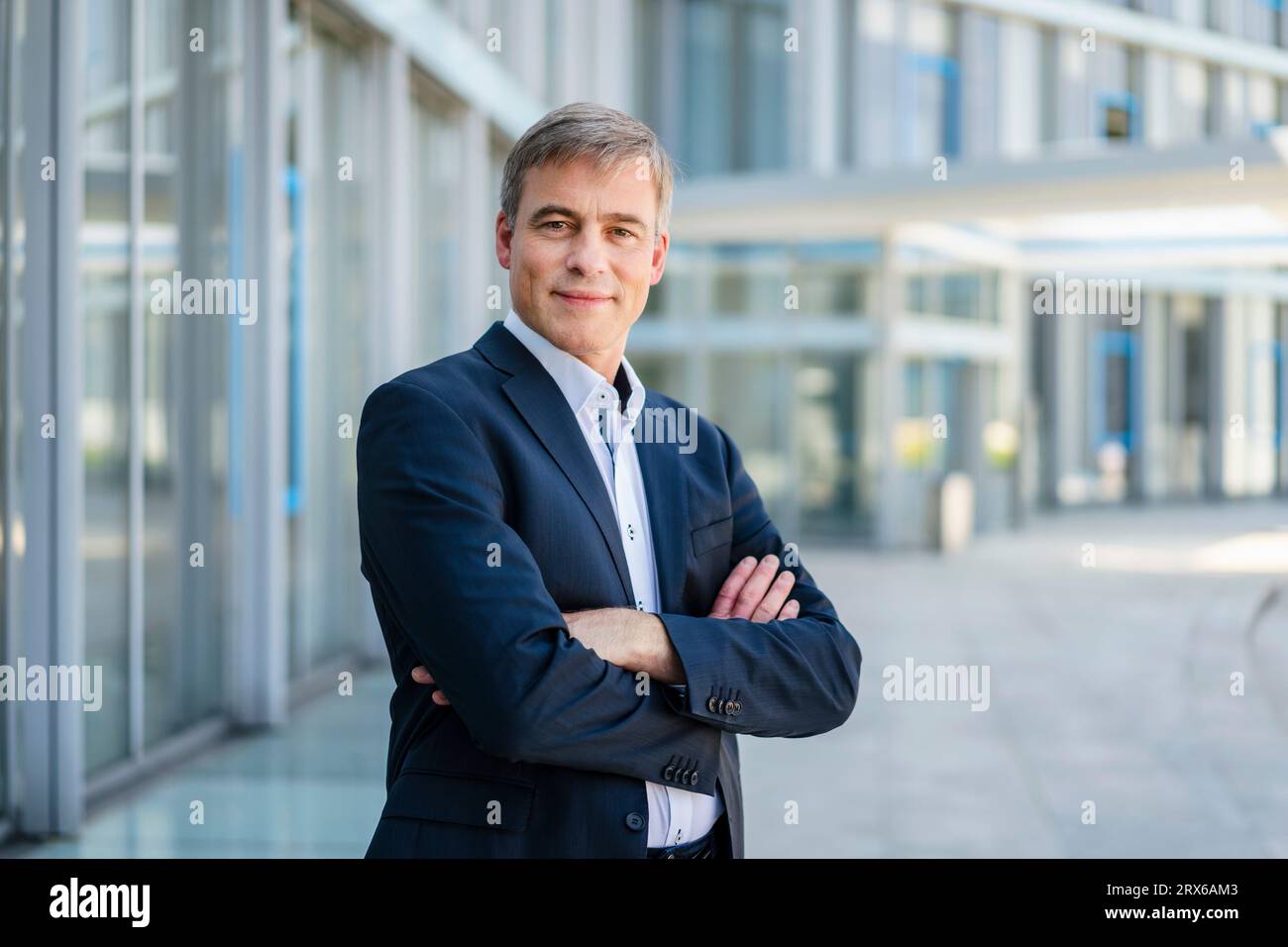 Uomo d'affari sicuro di sé in piedi nell'edificio degli uffici con le braccia incrociate Foto Stock