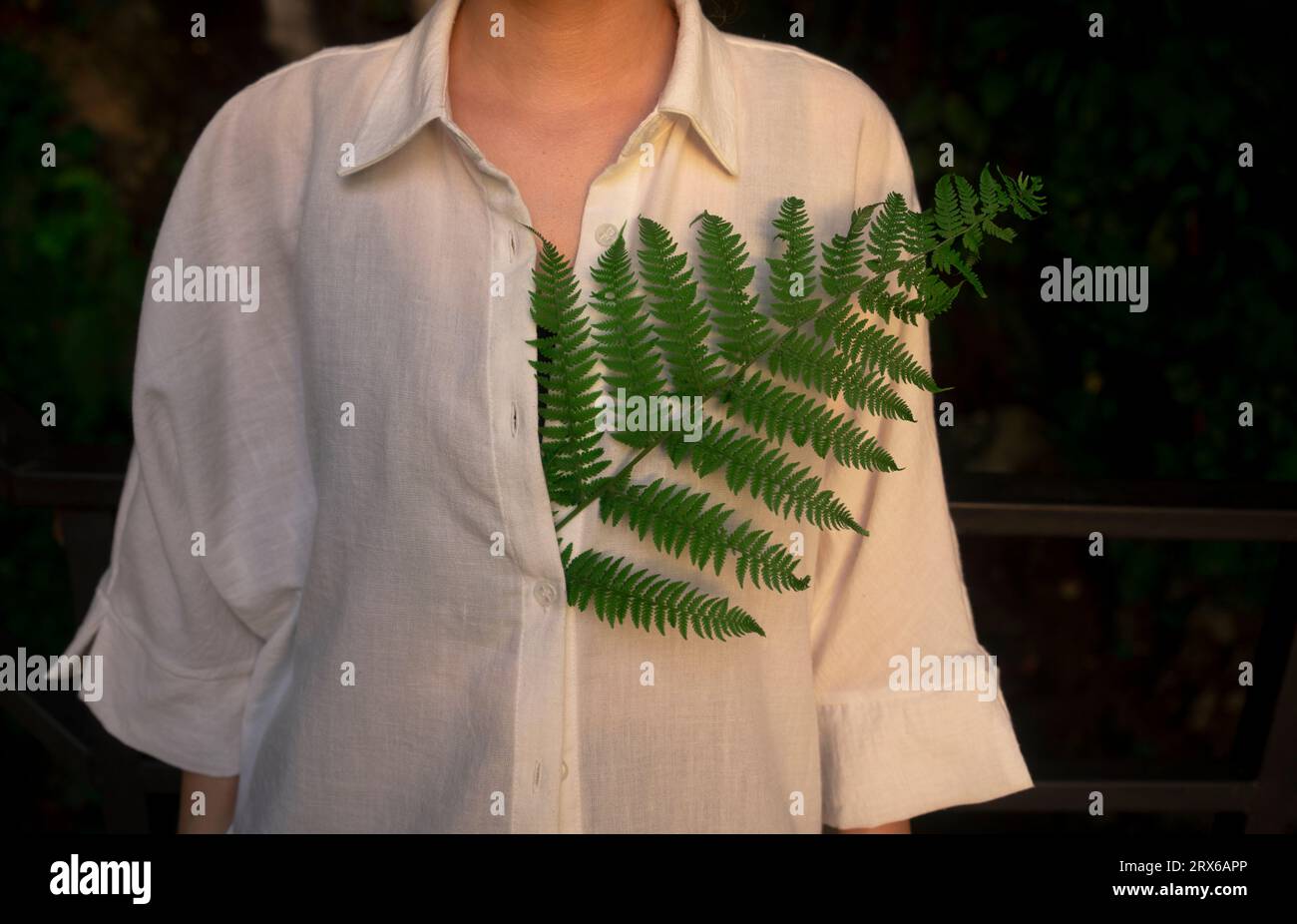 Donna con foglia di felce verde in camicia bianca Foto Stock