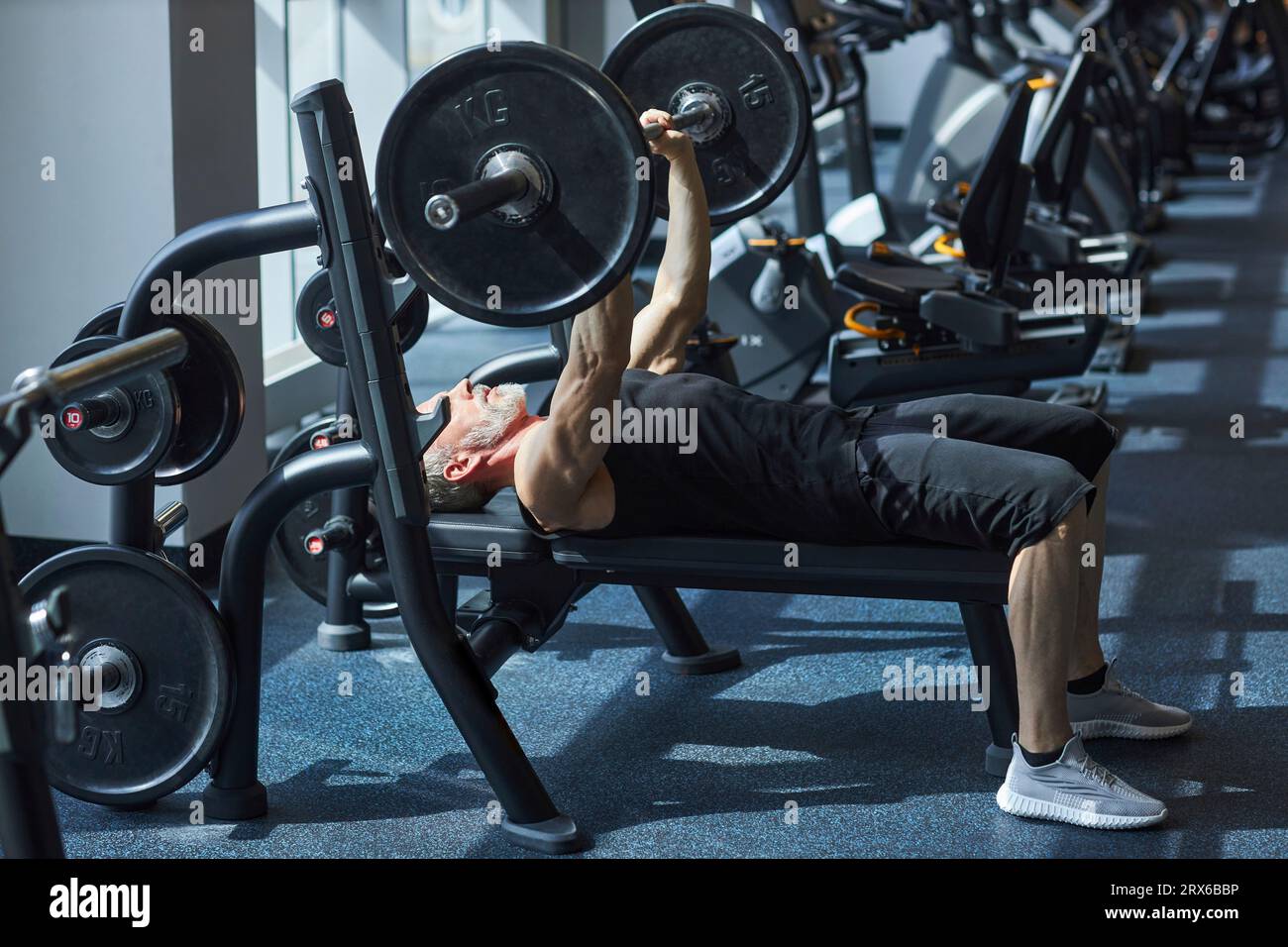 Uomo maturo che fa esercizio di panchina in palestra Foto Stock