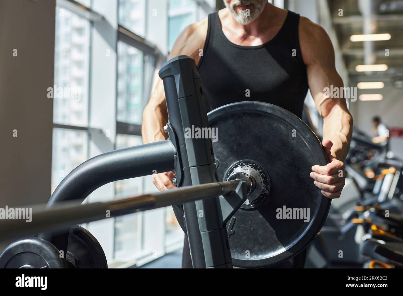Uomo maturo che prepara il campanello per la pressa da panchina in palestra Foto Stock