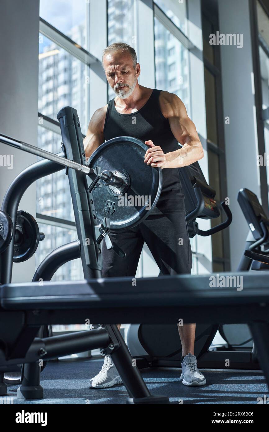 Uomo maturo che prepara il campanello per l'esercizio della pressa a panchina Foto Stock