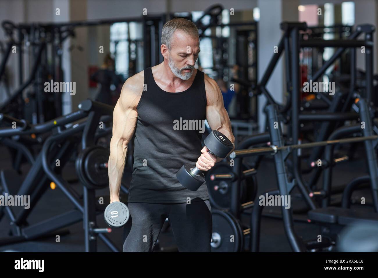 Uomo maturo forte che fa esercizio fisico con manubri in palestra Foto Stock