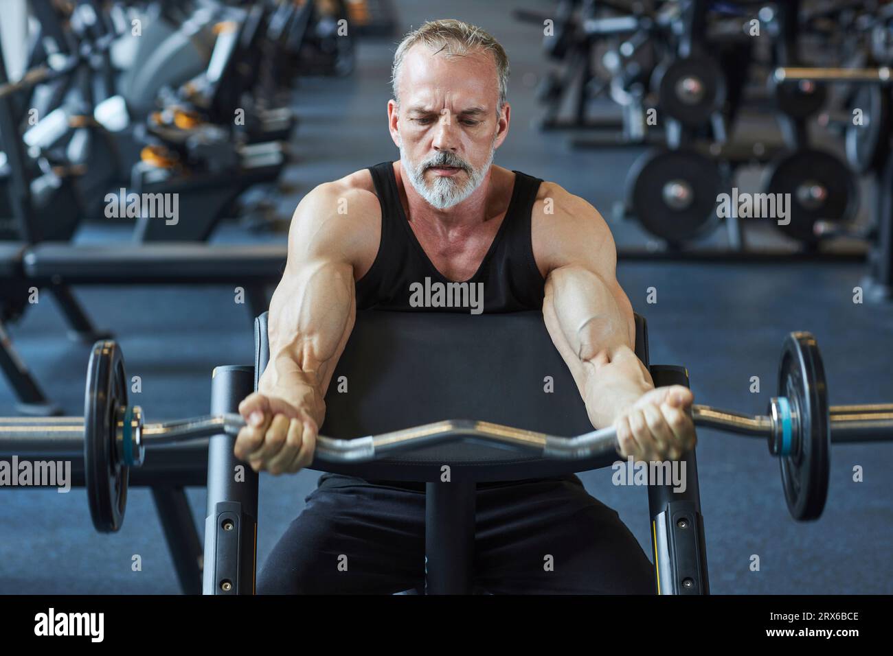 Uomo maturo che rinforza le braccia con il campanello in palestra Foto Stock