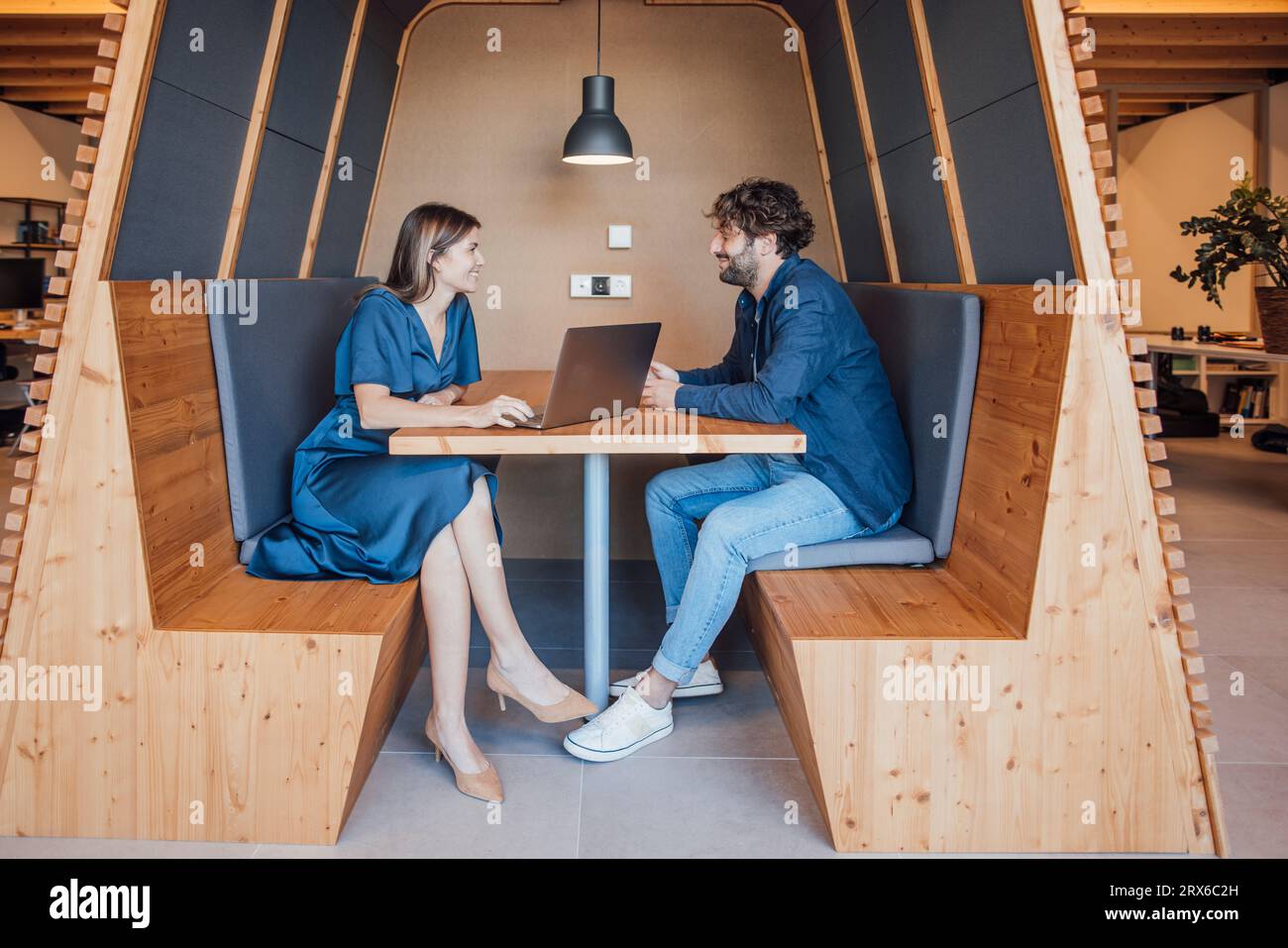 Persone d'affari felici sedute con un computer portatile e chiacchierate in ufficio Foto Stock