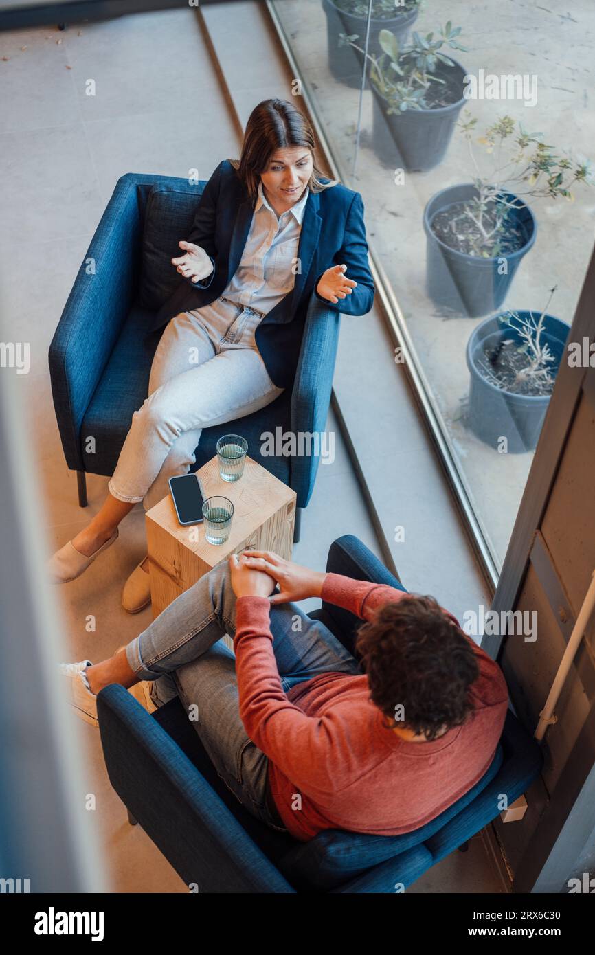Donna d'affari che discute con un uomo d'affari seduto in poltrona Foto Stock