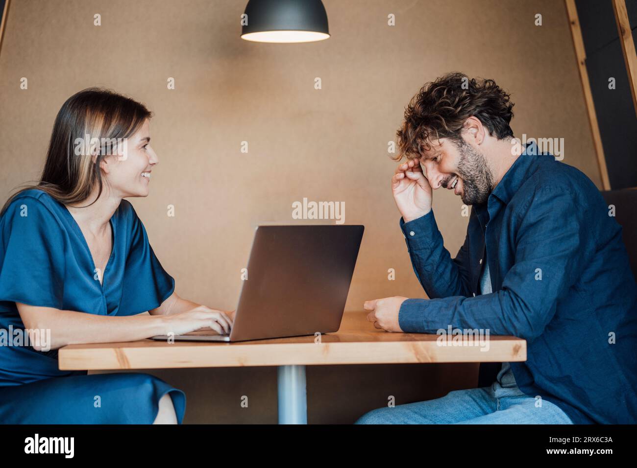Donna d'affari sorridente che usa un computer portatile e parla con un uomo d'affari nell'ufficio Foto Stock